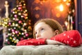 Red-haired girl dreams of near the Christmas tree. smiles, garland, lights, festive, new year Royalty Free Stock Photo