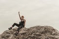 Red-haired girl gestures with a middle finger sitting on the stones above the precipice against the backdrop of mountains and Royalty Free Stock Photo