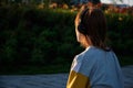 Red-haired girl with headphones sits in the streets of sunset, frame from the back