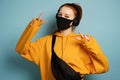 A red-haired girl with headphones, yellow hoodie, protective mask, stands and shows the mark of the world with hands Royalty Free Stock Photo