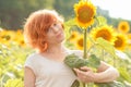 red-haired girl hugging a tall sunflower at sunset, young redheaded woman in the field of sunflowers hugging a sunflower, funny s Royalty Free Stock Photo