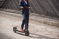 A red-haired girl in a jacket and trousers drives an electric scooter along the wall. A business woman in a pantsuit and