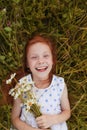 A red-haired girl lies on the grass with a bouquet of daisies in her hands and laughs Royalty Free Stock Photo