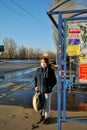 A red-haired girl in a medical mask stands at a public transport stop on a sunny spring evening.