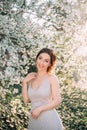 Red-haired girl in a modest, gray dress in rustic style. Portrait of the bride on the background of a blossoming tree