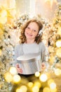 Red-haired girl opens a gift near the Christmas tree. smiles, garland, lights, festive, new year Royalty Free Stock Photo