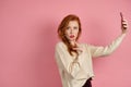 A red-haired girl with red lipstick stands on a pink background in a half-turn and wistfully looks into the frame Royalty Free Stock Photo