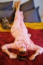 Red-haired girl in red pajamas on a red bed at home next to pet. A woman listens to music on headphones with a cat during a Royalty Free Stock Photo
