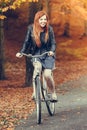 Red haired girl riding on bike in autumnal park Royalty Free Stock Photo