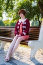 Red haired girl in a short pink dress on a park bench