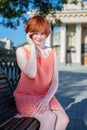 Red haired girl in a short pink dress on a park bench