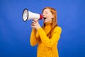 Red-haired girl shouting into a megaphone news on a blue studio background