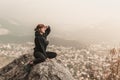 Red-haired girl is sitting on the stones above the precipice against the backdrop of mountains and fog Royalty Free Stock Photo