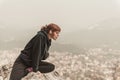 Red-haired girl is sitting on the stones above the precipice against the backdrop of mountains and fog Royalty Free Stock Photo