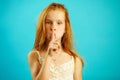 Red haired girl with strict look puts her finger to lips, demonstrates secret and confidentiality, does not tell anyone
