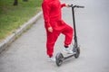 Red-haired girl in a red tracksuit drives an electric scooter. A young woman in oversized clothes rides around the city