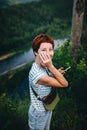 Red-haired hipster girl with a phone, stands against the background of the river. Processing under the film.