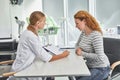 Red-haired lady looking at clipboard while sitting at the table with doctor Royalty Free Stock Photo