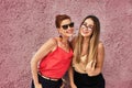 A red-haired laughing middle-aged woman in a red blouse and glasses and a young laughing woman with brown hair in a golden blouse