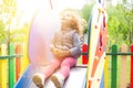 Red-haired little girl sits on a childrens slide in the park and looks into the bright sky Royalty Free Stock Photo