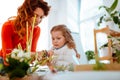 Red-haired mom cutting dry edges of home plant with daughter