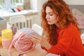 Red-haired needlewoman looking at nice light purple thread