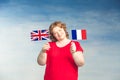 Red-haired plump woman holding French and British flags in front of him on a blue background