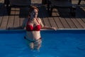 A red-haired pregnant woman in a red bikini is resting in the pool, leaning on the side. Royalty Free Stock Photo