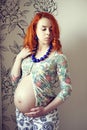 Red-haired pregnant woman with blue beads on her neck in the studio