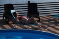 Red-haired pregnant woman in a red bikini sunbathes lying on a sun lounger next to the pool. Royalty Free Stock Photo