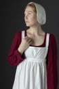 A Regency maid servant wearing a red linen dress with an apron and cap against a studio backdrop