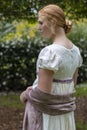 Regency woman in cream dress walks alone in a summer garden