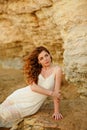 The red-haired sensual girl in white dress sitting on the rocks Royalty Free Stock Photo