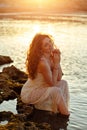 The red-haired sensual girl in white dress sitting on the rocks Royalty Free Stock Photo