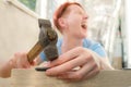 Red-haired, short-haired woman screams in pain, striking herself on the finger with a hammer