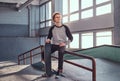 Young red-haired skateboarder holding his board while sitting on a grind rail in skatepark indoors. Royalty Free Stock Photo