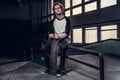 Young red-haired skateboarder holding his board while sitting on a grind rail in skatepark indoors. Royalty Free Stock Photo