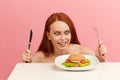 Red-haired skinny woman with greedy eyes being ready to eat burger.