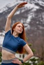 Red-haired Sportswoman warming up before jogging outdoor, concentrated on sport