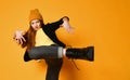 Red-haired teen girl in knitted hat, yellow t-shirt, jeans and brutal shoes is dancing cool holding leg up