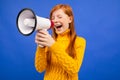 Red-haired teenage girl screaming with closed eyes to the news loudspeaker on a blue studio background