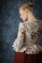 Red-haired 18th century woman standing in front of baroque wall paper Royalty Free Stock Photo