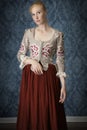 Red-haired 18th century woman standing in front of baroque wall paper Royalty Free Stock Photo