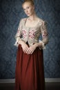 Red-haired 18th century woman standing in front of baroque wall paper Royalty Free Stock Photo