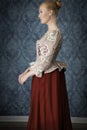 Red-haired 18th century woman standing in front of baroque wall paper Royalty Free Stock Photo