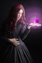 Red-haired woman in a black Victorian ensemble and a witch-like pose. An orb of light is in her hand.