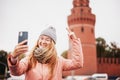 Red-haired woman in glasses traveler in a hat and jacket chatting on a smartphone while taking a selfie in Moscow, on Kremlin