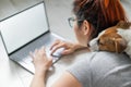 Red-haired woman in isolation lying on the floor with a dog. The girl maintains a social distance and works from home on