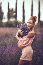 Red-haired woman in jumpsuit with shorts stands in the middle of field with bouquet of lavender looking at camera Royalty Free Stock Photo