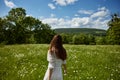 a red-haired woman in a light dress stands in a chamomile field with her back to the camera Royalty Free Stock Photo